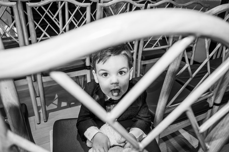 Black-and-white candid of a young boy peering out from inside a playground climbing frame