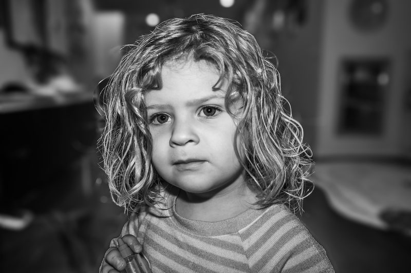 Black-and-white portrait of a curly-haired young child looking directly at the camera