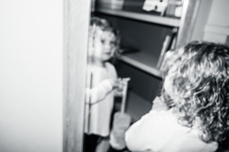 Black-and-white documentary frame of two young children playing around a doorway at home