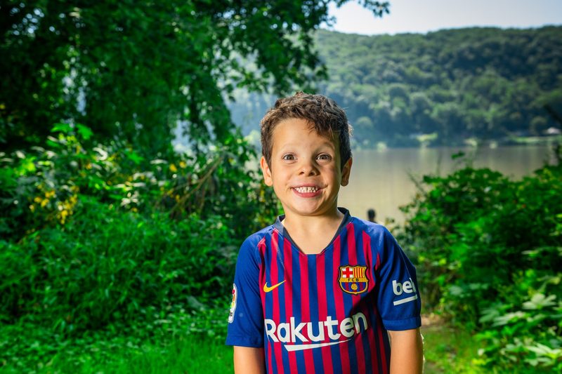 Boy in a striped soccer jersey grinning at the camera with the river behind him