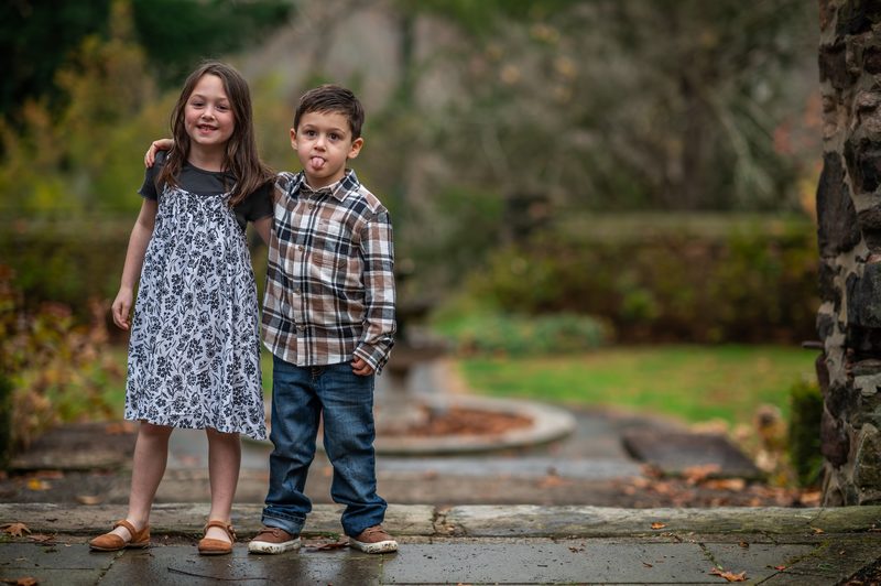 A brother and sister standing together on a garden path during a Philadelphia family portrait session