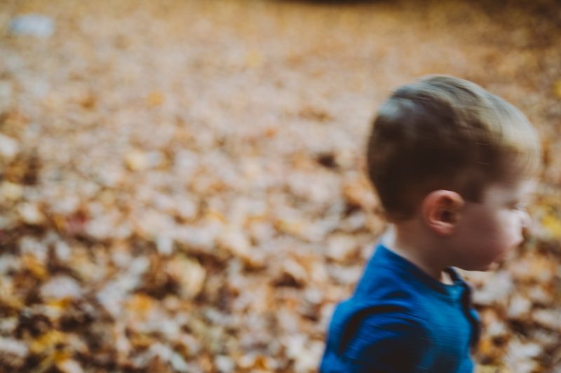 Young boy photographed through a blur of falling autumn leaves