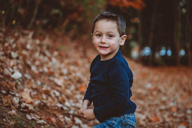 Portrait of a young boy in a navy sweater on an autumn trail covered in orange leaves near Philadelphia