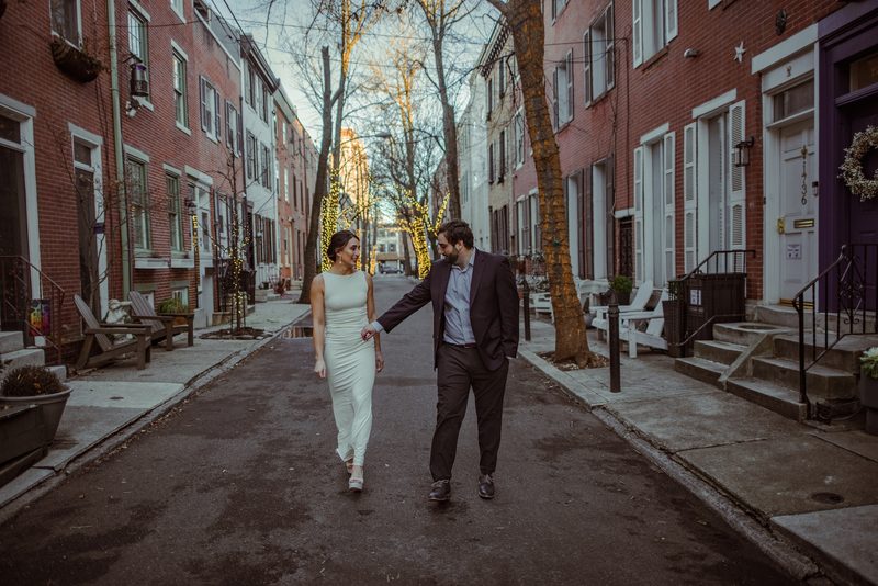 Engaged couple walking hand in hand down a cobblestone Philadelphia street at dusk