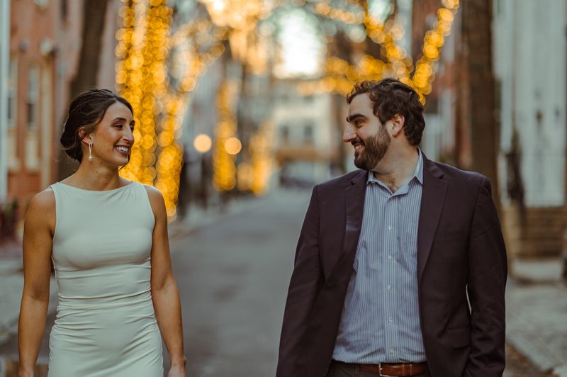 Couple walking a cobblestone street under warm string lights during a Philadelphia engagement session