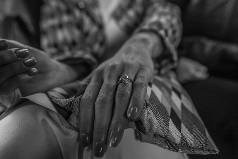 Black-and-white detail of an engagement ring on a woman's hand resting in her lap