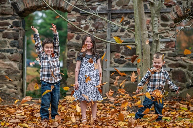 Three kids throwing autumn leaves in the air in front of a stone wall during a Philadelphia family photo session