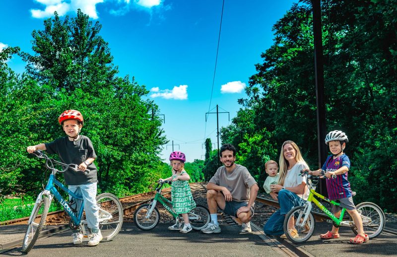 Family of six with three kids' bikes lined up at a railroad crossing under a bright blue summer sky