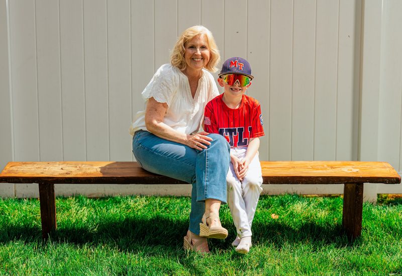 Grandmother and her grandson in a baseball cap sitting together on a bench in summer