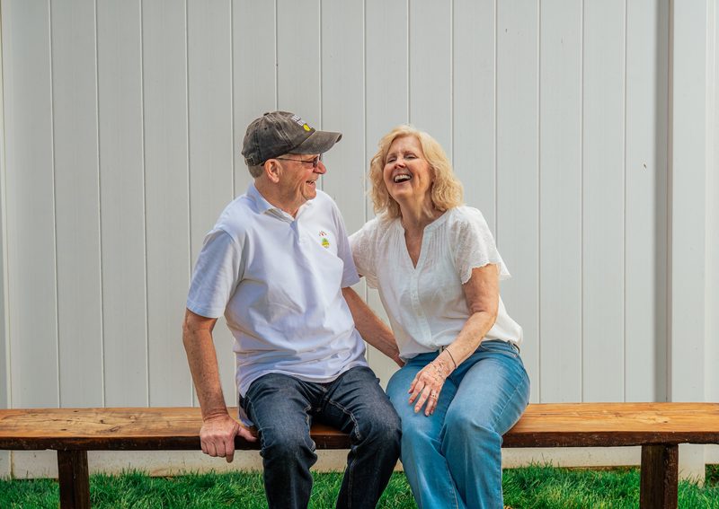 Grandparents sitting on a bench laughing together during a summer extended-family session