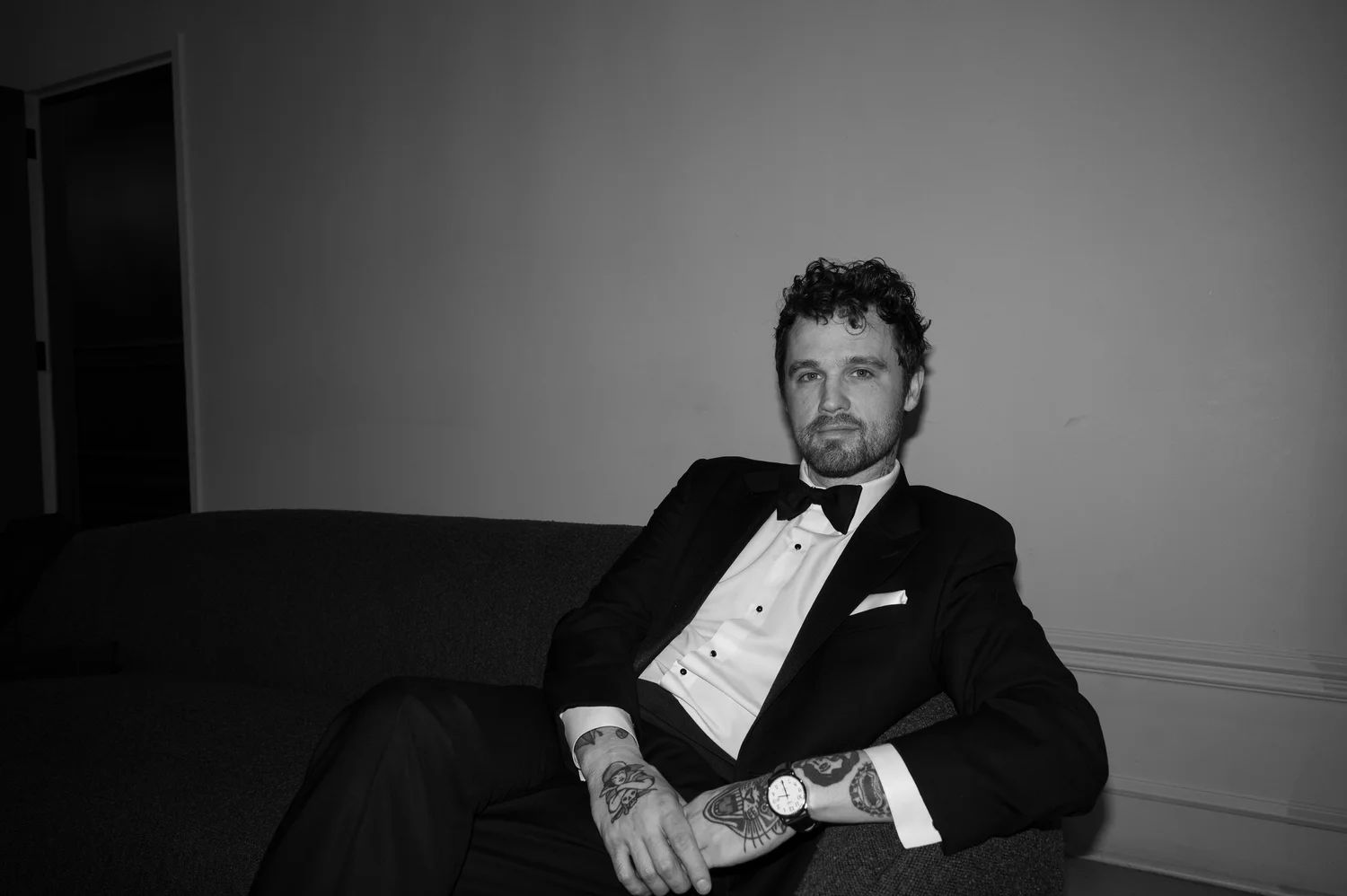 Black-and-white portrait of Joshua, founder of Cowdog Studio, seated on a sofa in a tuxedo