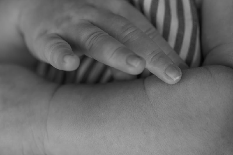 Detail photograph of an adult hand resting on a sleeping newborn in a striped sleepsuit