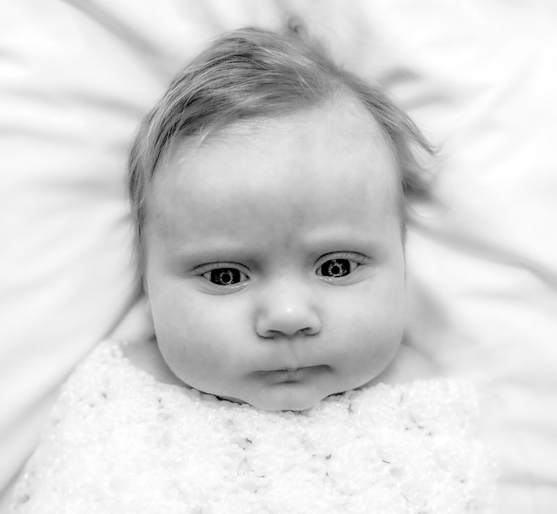 Black-and-white close-up of a newborn's face, wide-eyed, wrapped in a white knit blanket