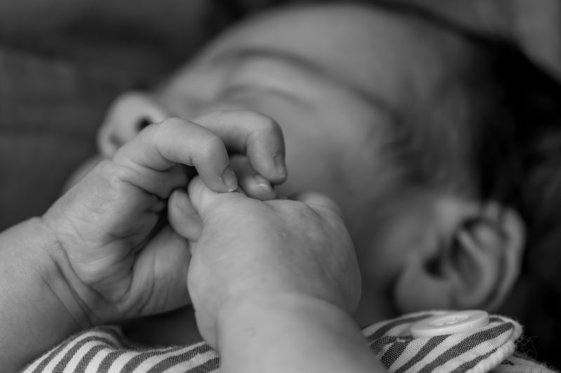 Newborn baby gripping a parent's finger, photographed in black and white