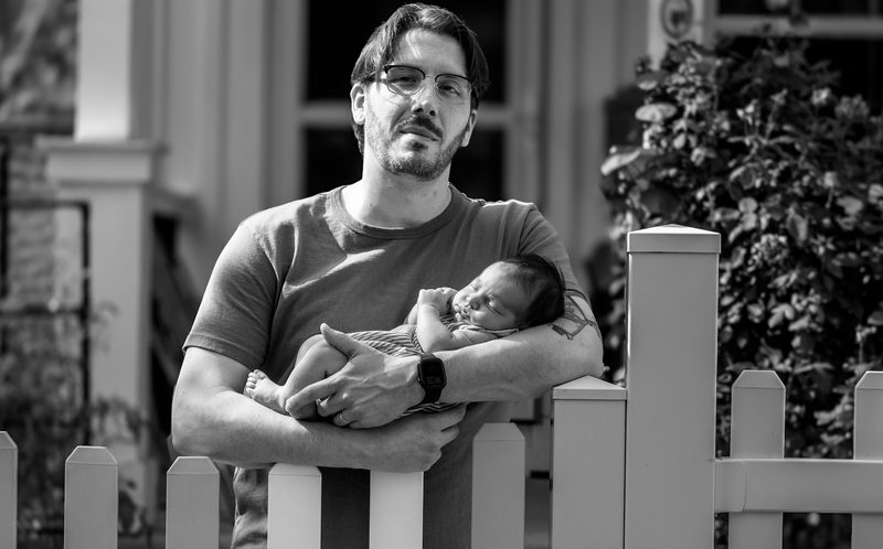 Black-and-white photograph of a father holding his newborn on a Philadelphia porch