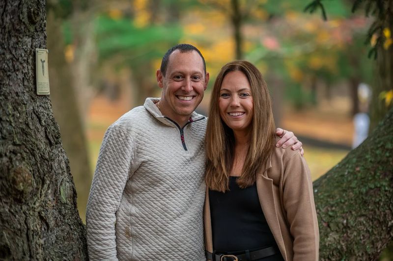 Parents standing together between two trees in an autumn park during a Philadelphia family session