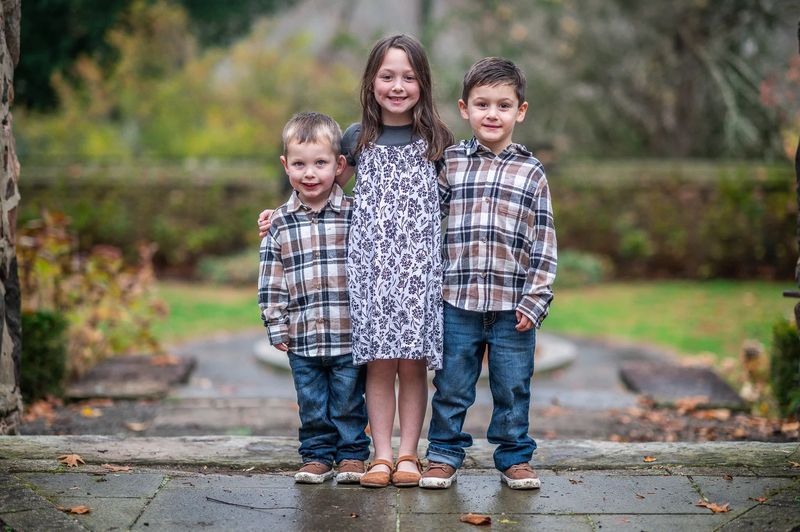 Portrait of three siblings in matching plaid standing together on a stone path in a Philadelphia garden