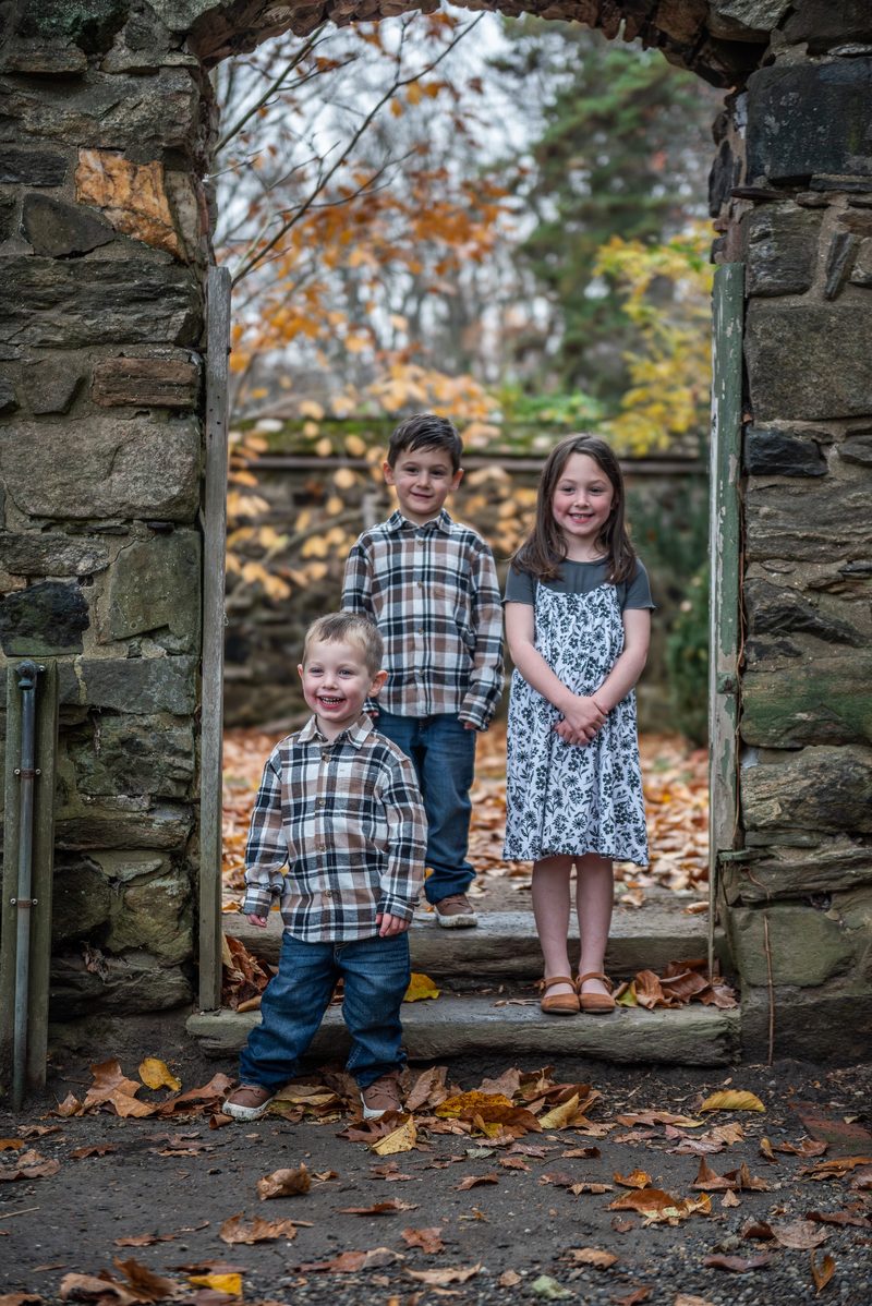 Three siblings framed in a stone archway surrounded by autumn leaves